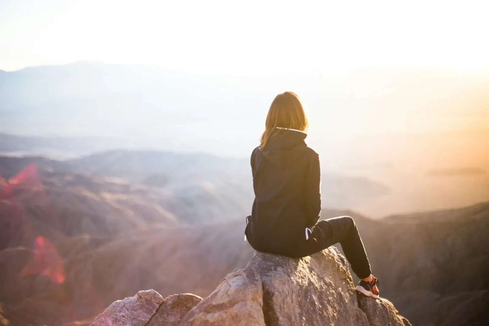 A person sitting on a rock watching the sun rise over the mountains